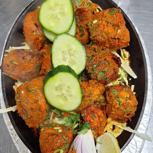 Sizzling chicken tikka with cucumber slices, onions, and lemon on a hot plate.