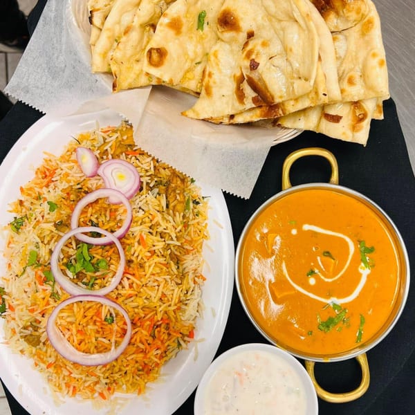Indian meal with biryani, naan bread, butter chicken, and raita on a black tablecloth.