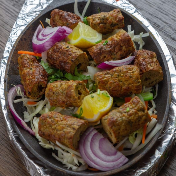 Sizzling platter of seekh kebabs with lemon wedges, red onion, and shredded cabbage.