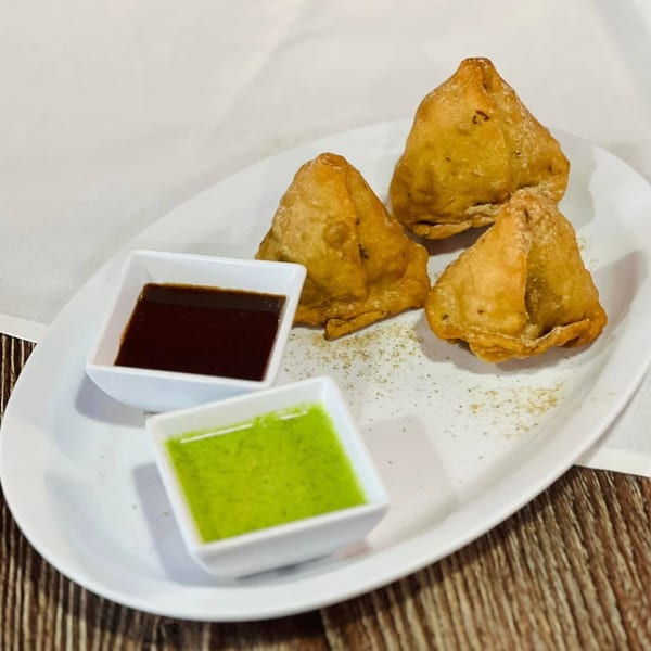 Three golden-brown samosas with two dipping sauces, one green and one brown, on a white plate.